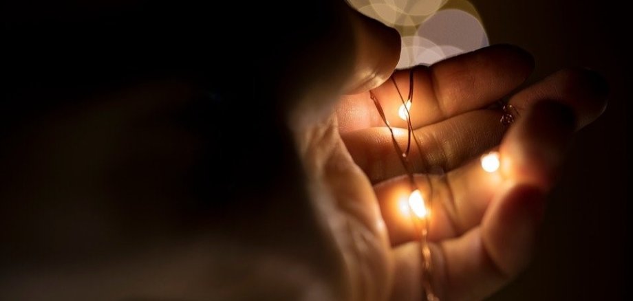 Eine gebogene Hand in der sich eine Lichterkette befindet. Im Hintergrund sieht man reflektiertes Licht der Lichterkette in form von kreisen.