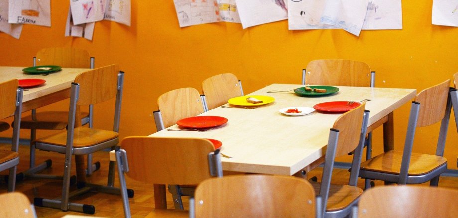 Ein Ess-Bereich in einem Kindergarten mit bunten Tellern auf den Tischen.