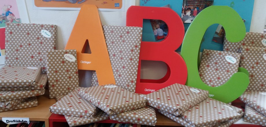 Die Buchstaben A,B,C stehen in Bunt an einer Wand angelehnt. Drumherum befinden sich die eingepackten Geschenke des Weihnachtsgewinnspiels der Bücherei Usingen, welche alle Beschriftet sind mit 1. bis 5. Klasse.