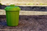 Grüne Miniatur-Mülltonne Grüne Miniatur-Mülltonne mit Deckel auf Straßenuntergrund