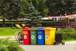 Verschiedenfarbige Mülltonnen nebeneinander Jeweils eine rote, grüne, blaue und gelbe Mülltonne mit kyrillischen Schriftzeichen nebeneinander in einem Park