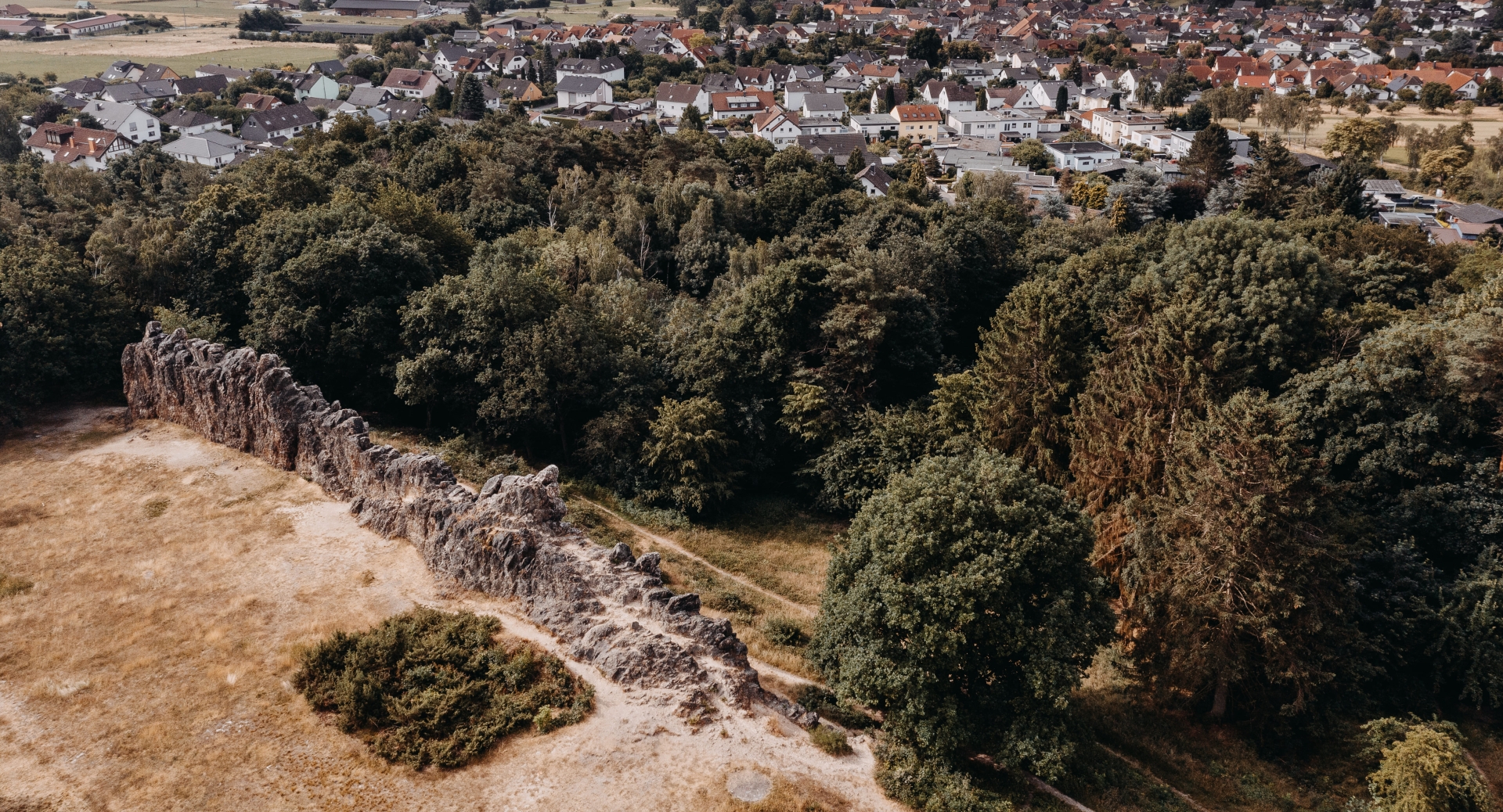 Eschbacher Klippen Luftaufnahme der Eschbacher Klippen mit einer langgestreckten Felsformation zwischen trockener Wiese und dichtem Wald. Im Hintergrund sind die Häuser der angrenzenden Ortschaft zu sehen.