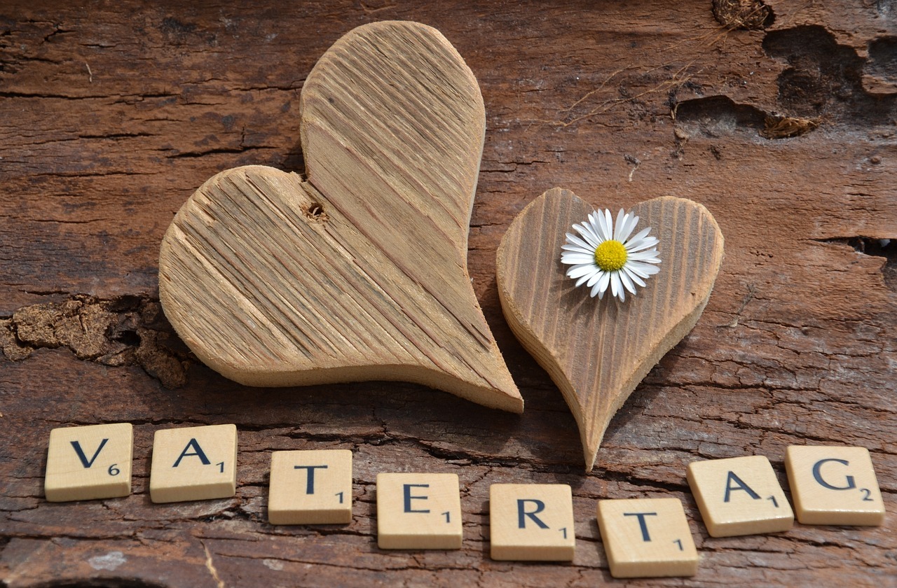 Vatertag Zwei Herzen aus Holz, darunter bilden Scrabble-Buchstaben das Wort Vatertag.