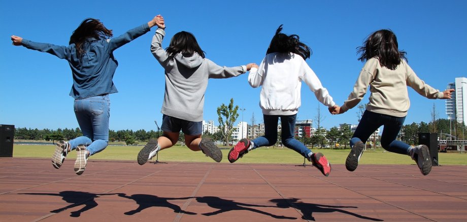 Vier Mädchen von hinten, welche in die Luft hüpfen