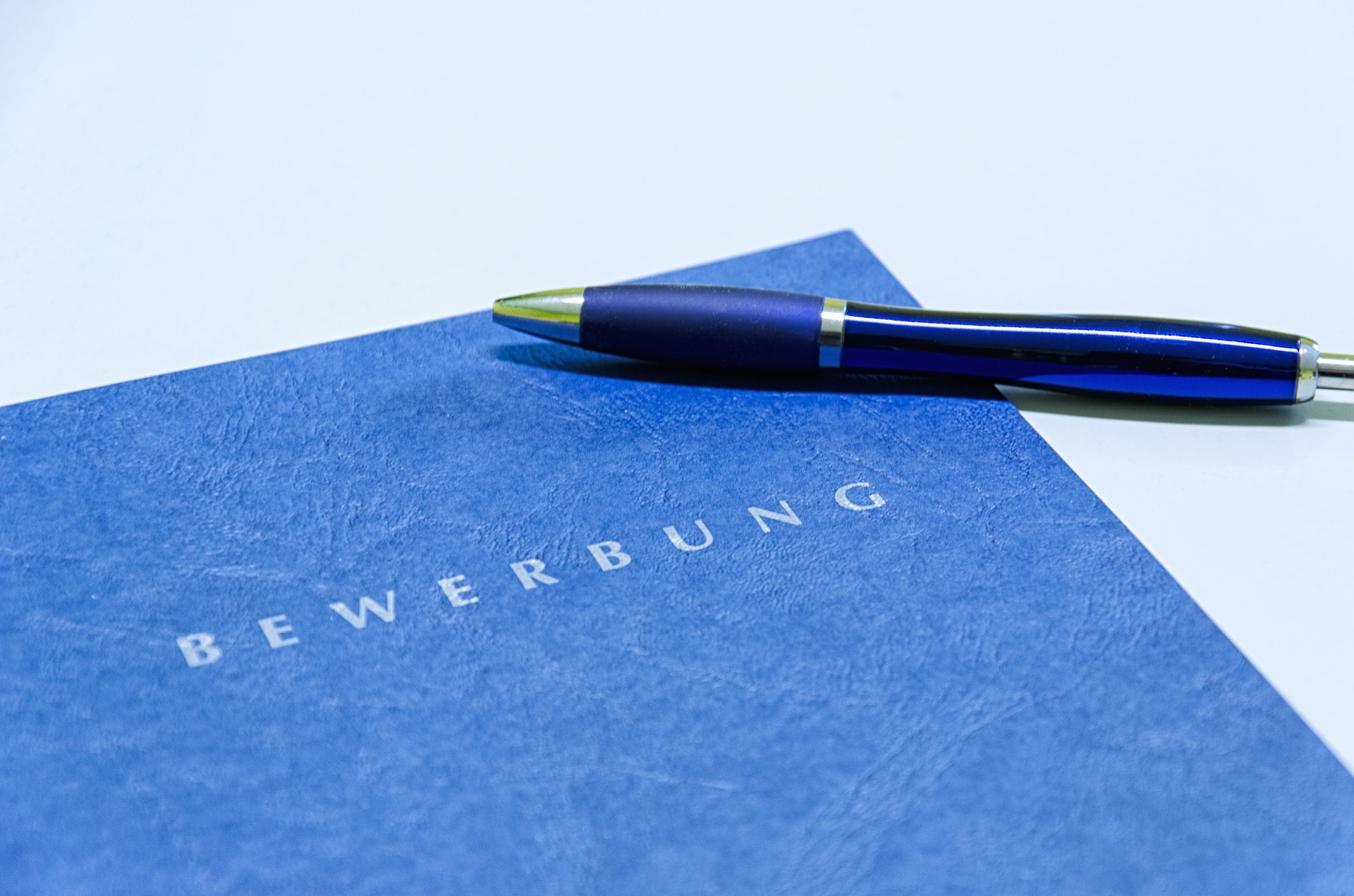 Eine blaue Bewerbungsmappe mit einem blauen Kugelschreiber oben drauf.