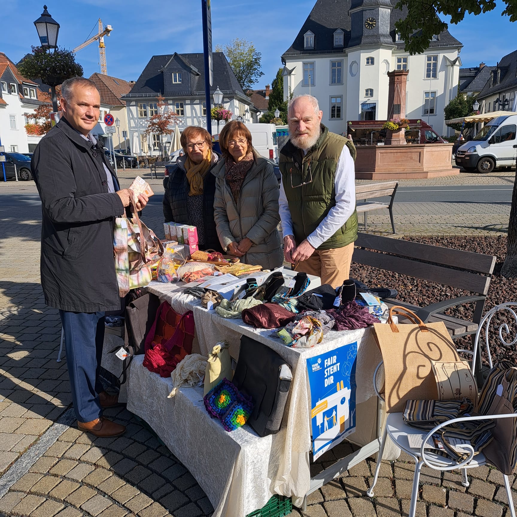 Auf diesem Foto sieht man vier Personen unter anderem links den Bürgermeister Steffen Wernard. Sie stehen an einem Marktstand, auf dem alten Marktplatz in Usingen. Der Marktstand bietet handgemachte Waren, wie Taschen, Schals und Accessoires.