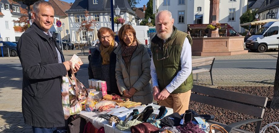 Auf diesem Foto sieht man vier Personen unter anderem links den Bürgermeister Steffen Wernard. Sie stehen an einem Marktstand, auf dem alten Marktplatz in Usingen. Der Marktstand bietet handgemachte Waren, wie Taschen, Schals und Accessoires.