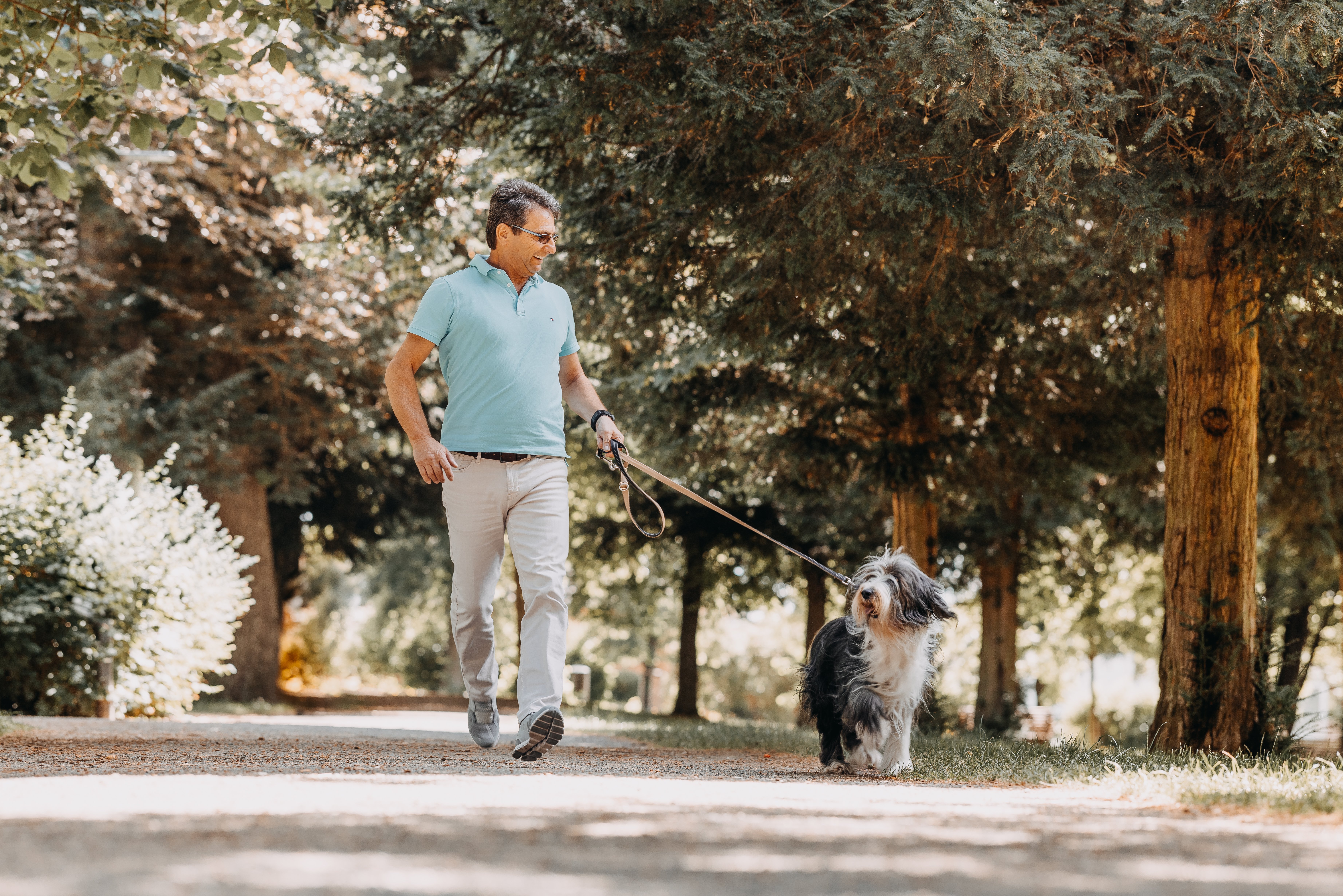Ein Mann der mit seinem Hund einen Spaziergang durch einen Park macht.