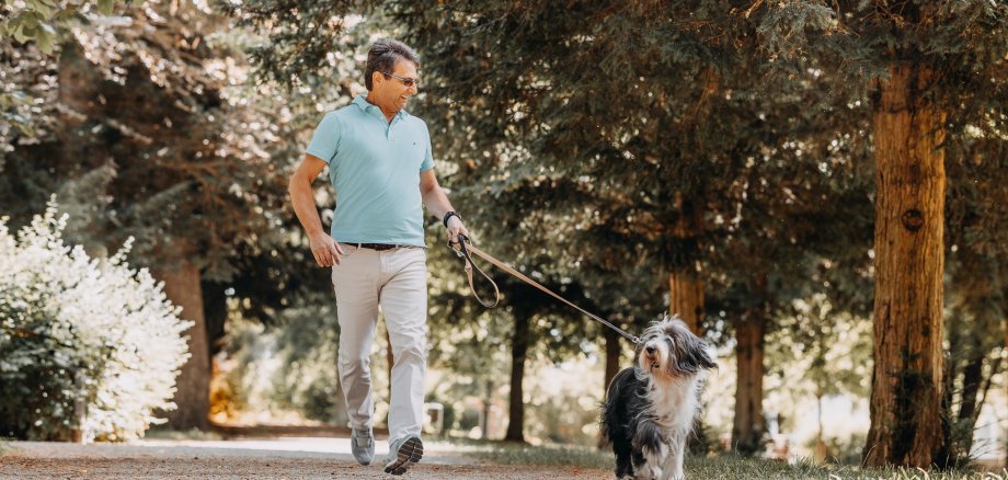 Ein Mann der mit seinem Hund einen Spaziergang durch einen Park macht.