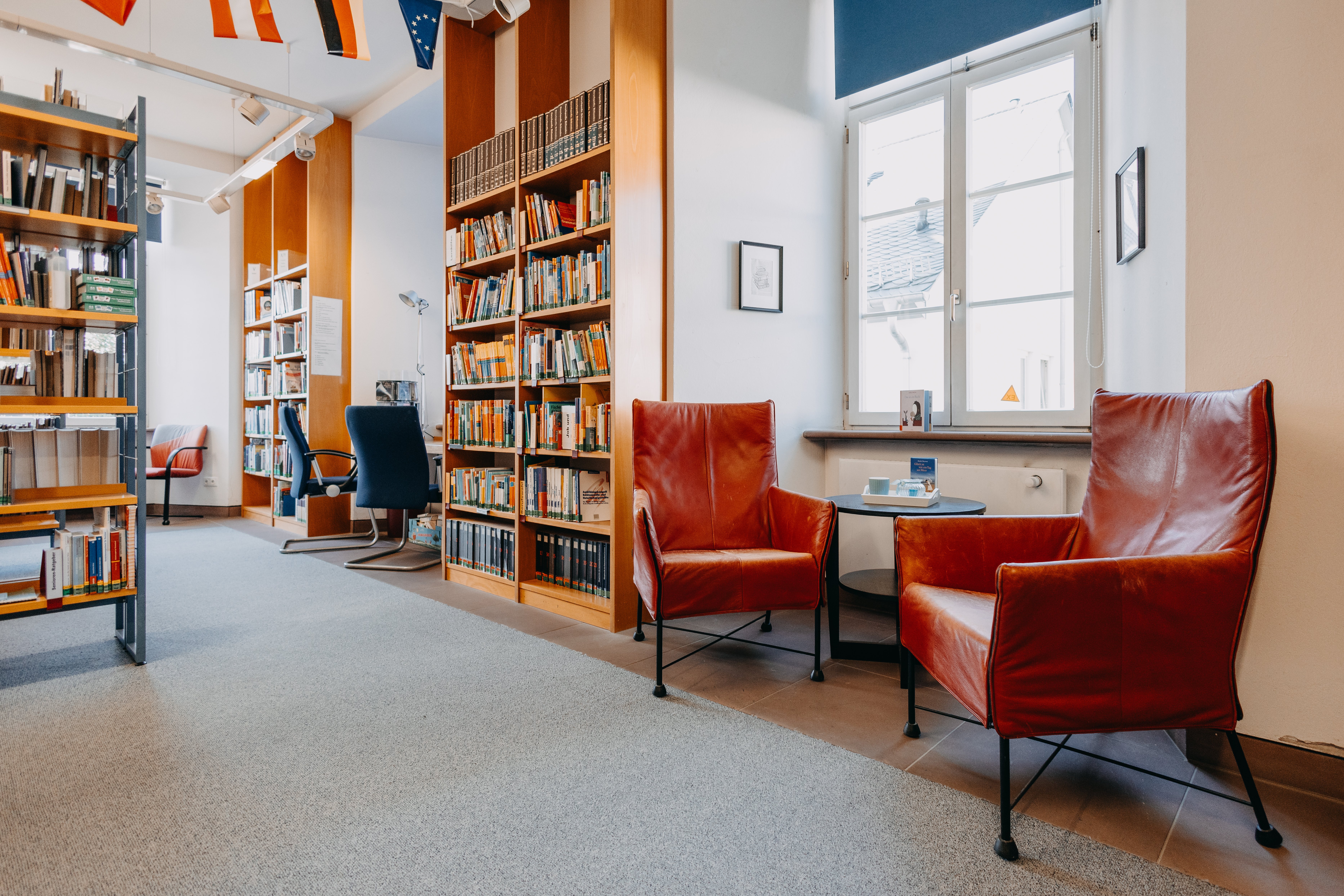 Zwei Sessel in der Stadtbücherei Usingen stehen unter einem Fenster. Zwei große Regale sind links auf der Seite zu sehen.