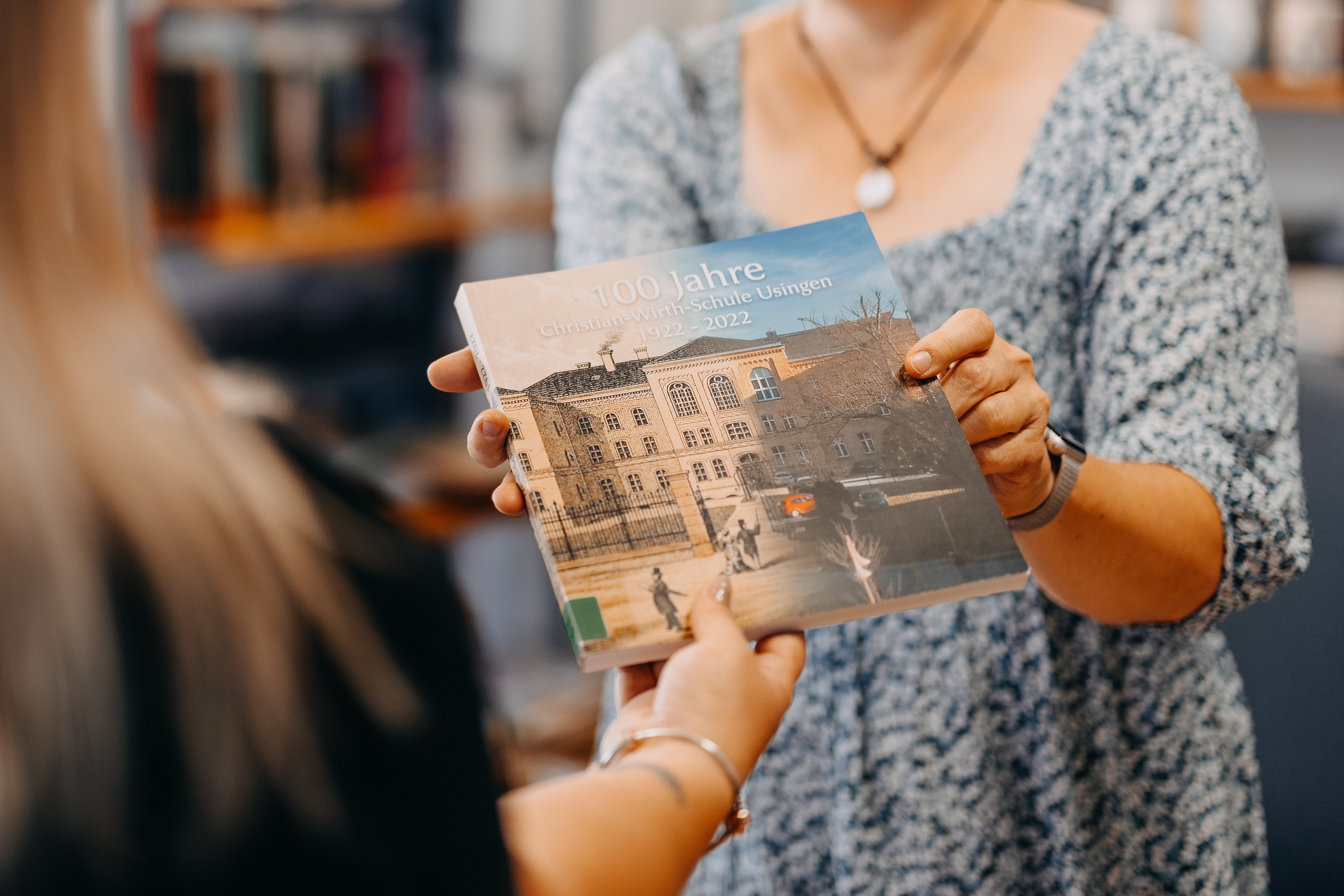 Zwei Frauen, welche ein Buch mit dem Titel "100 Jahre Christian Wirth Schule 1922-2022" halten.