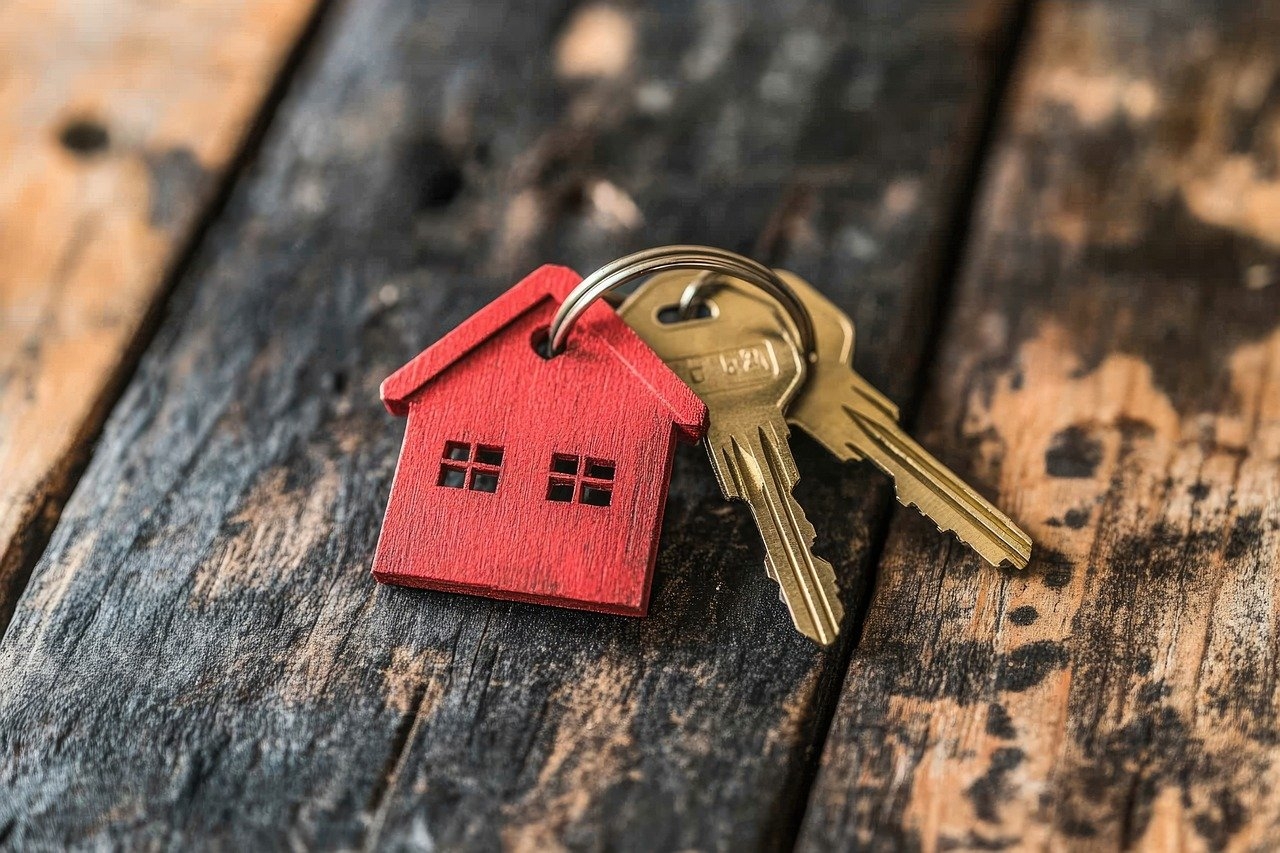 Ein goldener Schlüssel, mit einem roten kleinem Haus als Schlüsselanhänger, liegt auf einem Holztisch.