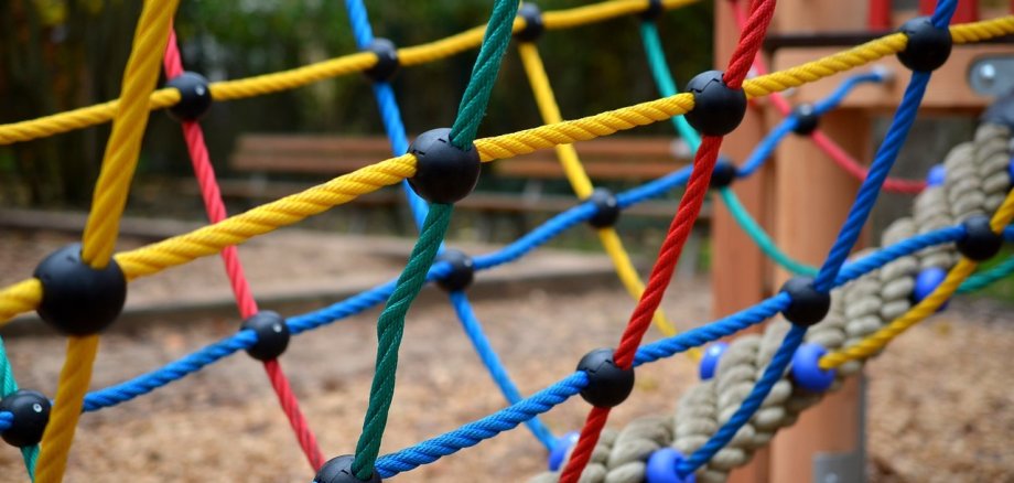 Ein Kinderspielplatz mit einer Bildaufnahme von einem buntem Kletterspielnetz.