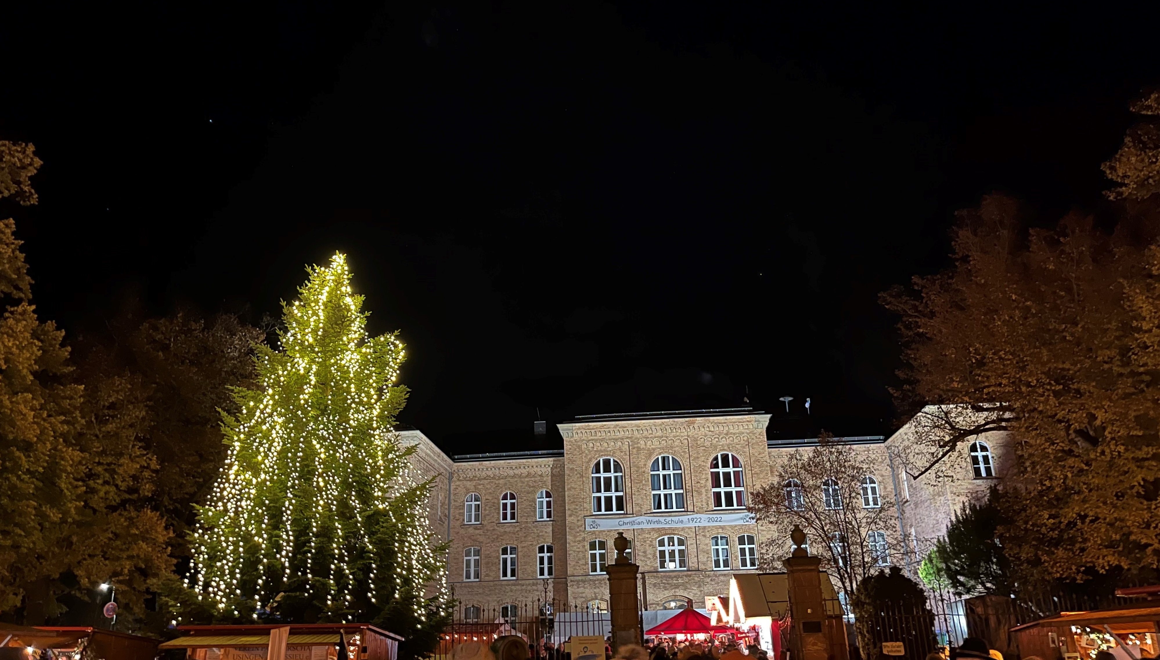 Blick auf die im Dunkeln beleuchtete CWS mit Weihnachtsbaum davor.