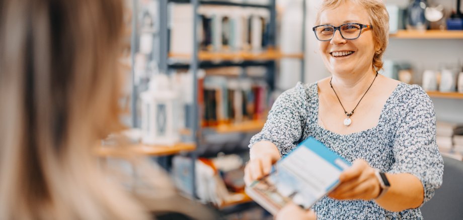 Zwei Frauen, welche sich ein Buch überreichen.