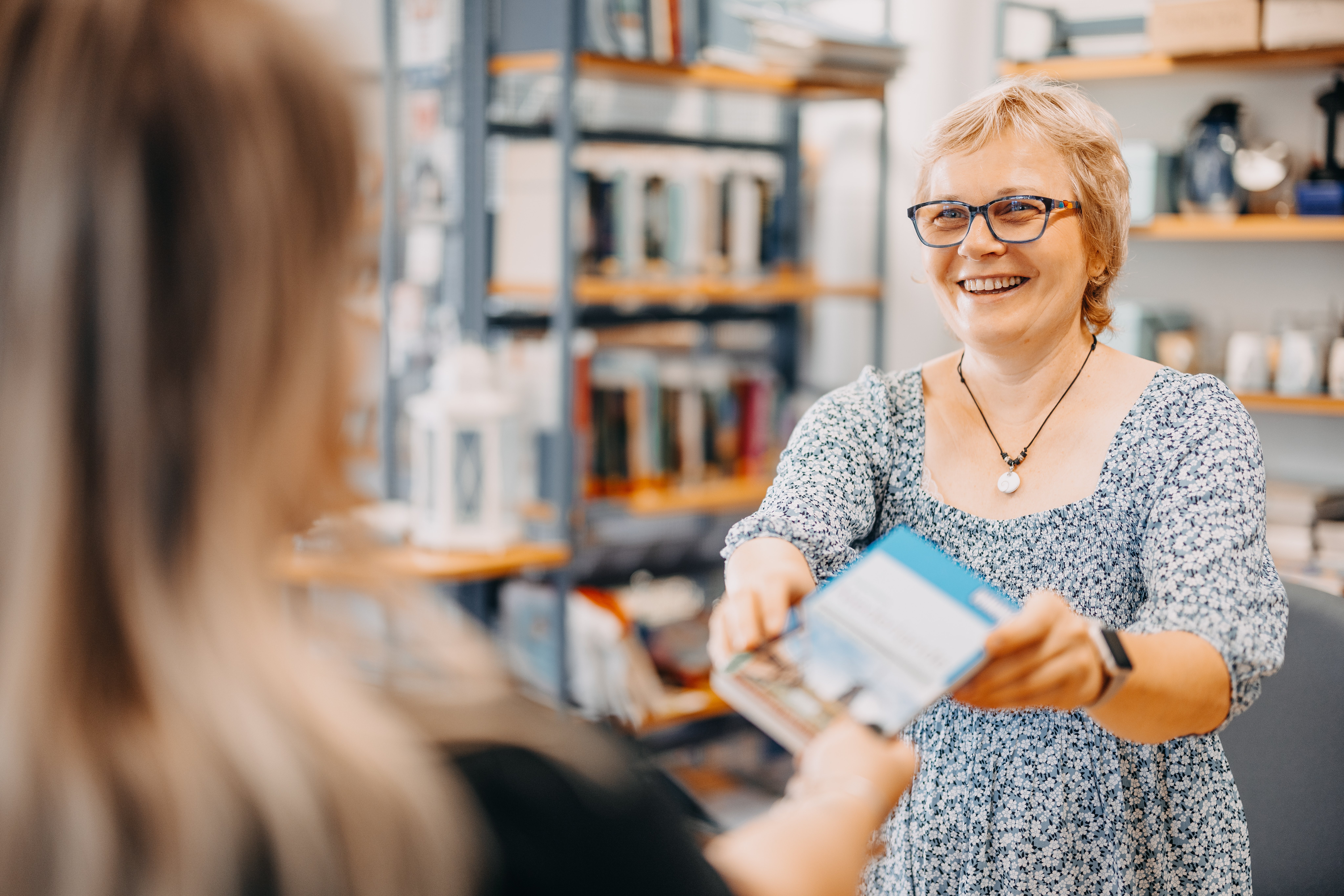 Zwei Frauen, welche sich ein Buch überreichen.