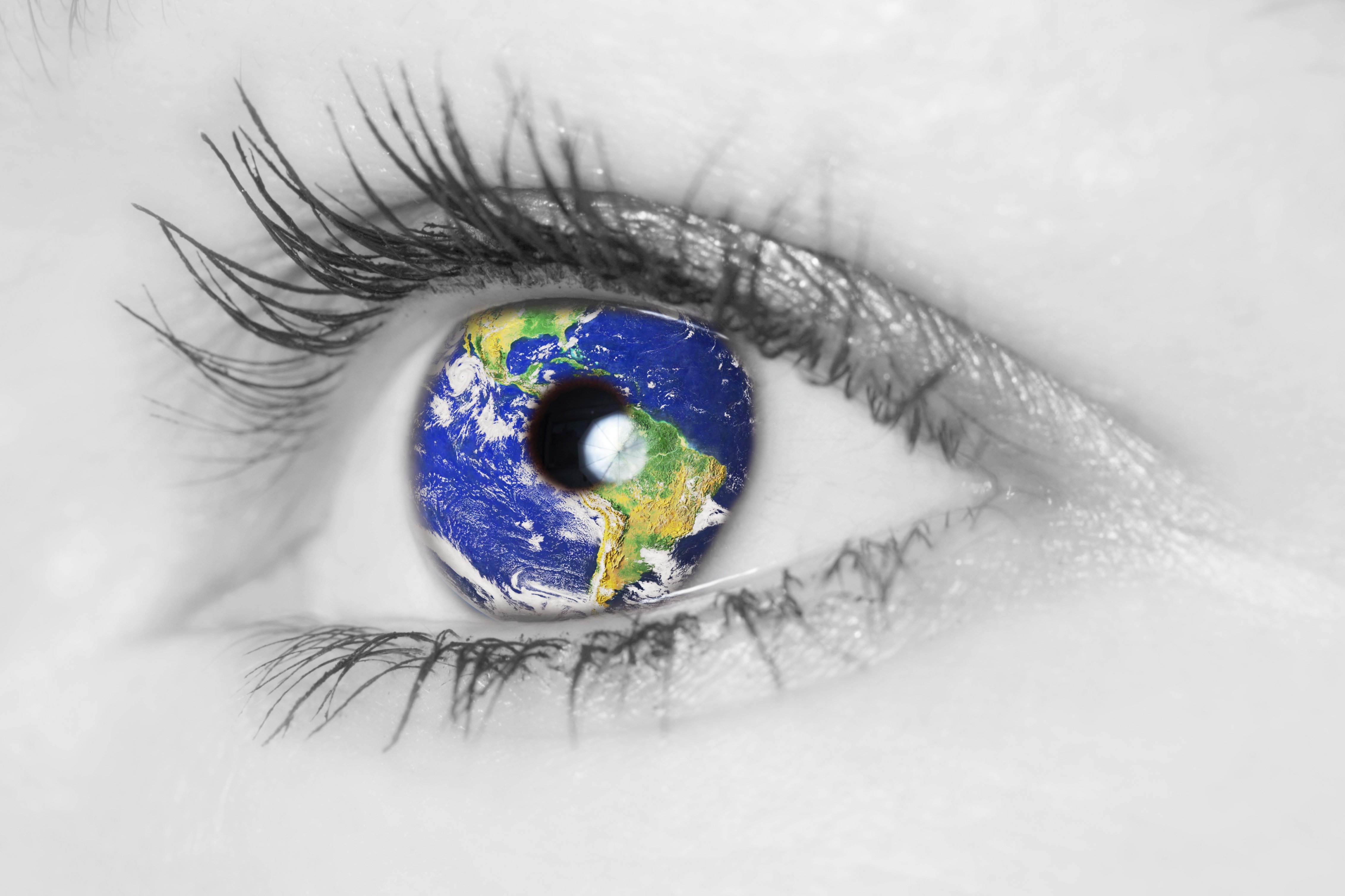 Schwarz-weiß Bild eines Auges in dessen Iris sich eine Weltkugel spiegelt.