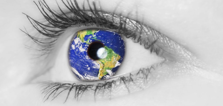 Schwarz-weiß Bild eines Auges in dessen Iris sich eine Weltkugel spiegelt.