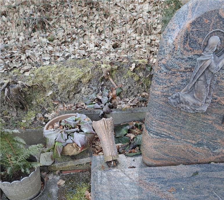 Zerstörte Vase an einem Grabstein.