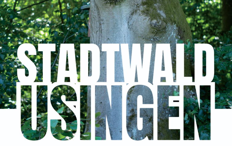 Schriftzug „Stadtwald Usingen“ vor einem Baumstamm und grünem Laub.