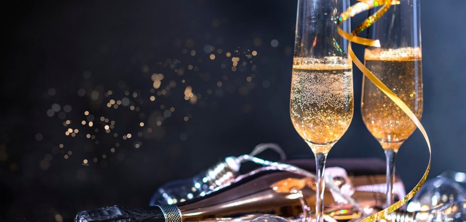 Sekt Zwei volle Sektgläser stehen auf goldenen Luftschlangen vor einem dunklen Hintergrund.