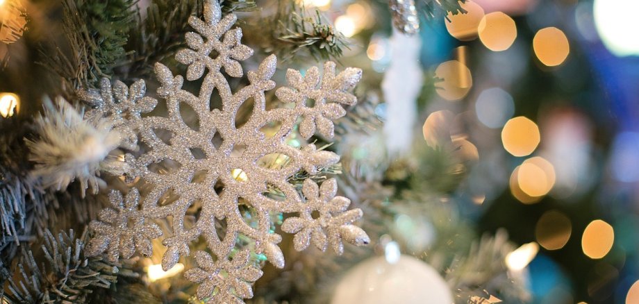 Geschmückter Tannenbaum mit einer Schneeflocke Eine große weiße, glitzernde Schneeflocke und Lichterketten im Hintergrund an einem Tannenbaum.