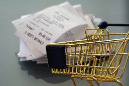 Einkaufswagen Im Vordergrund steht ein goldener Einkaufswagen. Im Hintergrund sieht man einen kleinen Stapel Kassenbons.