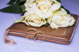 Hochzeit Zwei goldene Eheringe und weiße Rosen liegen auf einem Stammbuch.