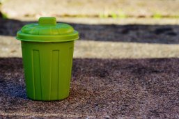 Grüne Mülltonne Eine kleine grüne Mülltonne mit Deckel steht auf Asphaltboden.
