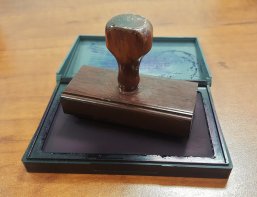Stempelkissen Ein Stempelkissen liegt auf einem braunen Holztisch. Auf dem Stempelkissen liegt ein Stempel.