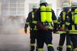 Vier Feuerwehrleute laufen in voller Ausstattung auf ein brennendes Gebäude zu.