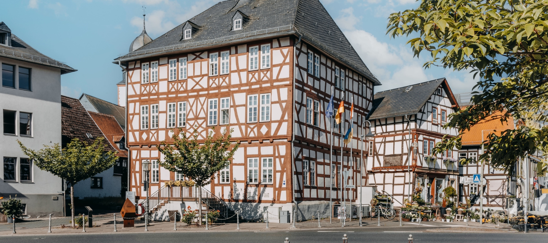 Historisches Rathaus in Usingen Historisches Rathaus in Usingen mit mehrgeschossiger Fachwerkfassade und Schieferdach. Vor dem Gebäude stehen mehrere Fahnen und kleine Bäume.